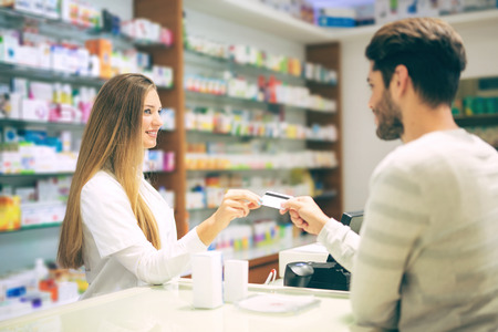 Experienced pharmacist counseling male customer in modern pharmacy and man pays with credit cardの写真素材