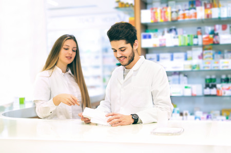 Pharmacist packing drugs at the pharmacy, female pharmacist helping himの写真素材