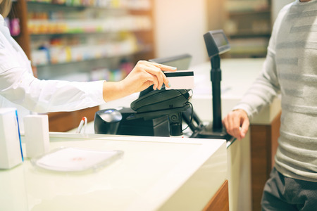 Woman at the pharmacy purchasing medicines and medical products she is inserting the credit card in the terminalの写真素材
