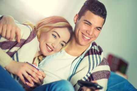 TV time. Young couple is drinking tea and using remote control to switch channels on the TV.の写真素材