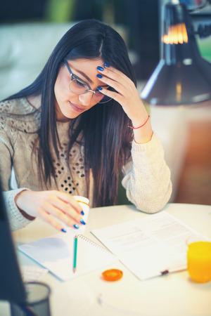 Young woman looking sick and tired sitting at home office table holding pill tablets.の写真素材
