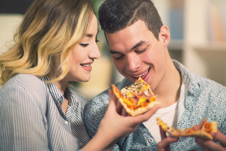 Couple relaxing at home and eating pizza.They are laughing and eating pizza and having a great time.の写真素材