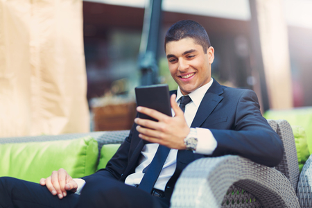 Young businessman sitting at an outdoor cafe using a digital tabletの写真素材