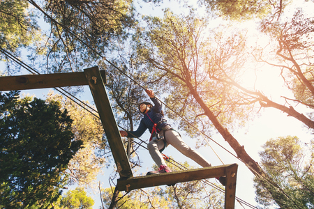 Happy school girl enjoying activity in a climbing adventure park on a summer day
