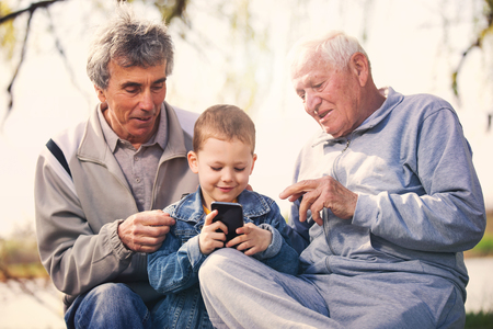 Two senior men and grandson using smart phone in the parkの写真素材