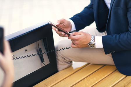 Close up of man on  solar bench charges phoneの写真素材