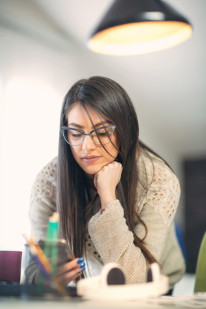 Woman leaning over the desk in home office using mobile phone.の写真素材
