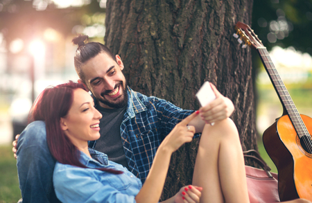 Loving couple holding each other sitting on a tree trunk on a romantic date in the park forestの写真素材