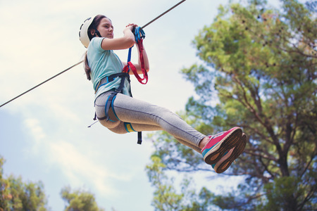 Happy school girl enjoying activity in a climbing adventure park on a summer dayの写真素材