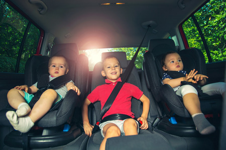 Three children in car safety seat - family, transport, safety, road trip and people conceptの写真素材