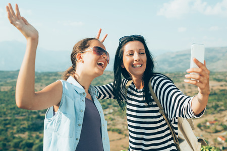 Mother and daugther photographing, taking a selfie on mountain peak, whilst restingの写真素材
