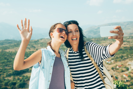 Mother and daugther photographing, taking a selfie on mountain peak, whilst restingの写真素材