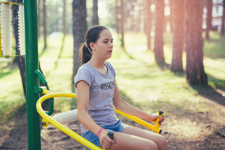 Young smiling teenage girl does exercises at massager simulator in parkの写真素材