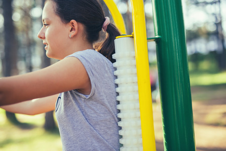 Young smiling teenage girl does exercises at massager simulator in park