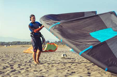 Handsome Caucasian man professional surfer standing in wetsuit on the sandy beach with his kite.の写真素材