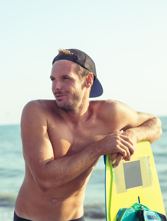 Smiling Caucasian man kitesurfer standing on the beach with his boardの写真素材