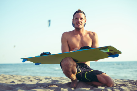 Smiling Caucasian man kitesurfer sittingg on the beach with hisboardの写真素材
