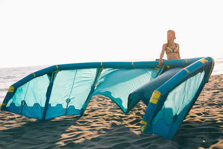 Pretty smiling Caucasian woman kitesurfer walking on the beach with her kiteの写真素材