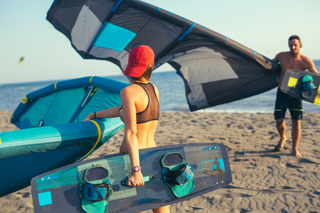 Pretty smiling Caucasian woman and man kitesurfer walking on the beach with their kiteの写真素材