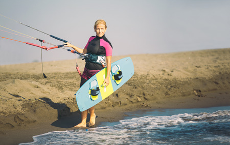 Beautiful Caucasian woman sufrer holding control bar and kiteboard and standing by the sea.の写真素材