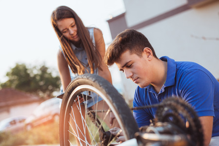 Teenager boy repair tire on bicycle , female friend standing next to him, using digital tablet for...