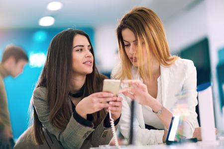 Two women is holding a mobile phone in store. They are looking for new smart phone.の写真素材