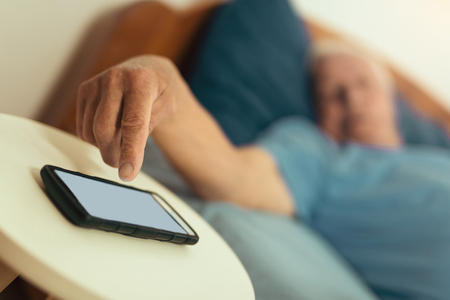 Senior man turn off wake-up alarm on the phone, focus on handの写真素材