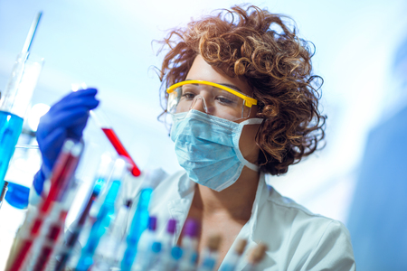 Woman is sitting at table in lab and holding blood test tubeの写真素材