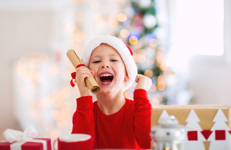Boy holding letter to Santa Claus in red hat near the Christmas treeの写真素材