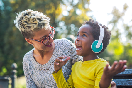 Smiling mother and little daughter having fun, listening to music on headphones. Mixed race family.の写真素材