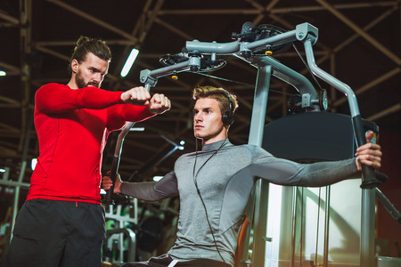 Young man and his personal fitness trainer in the gym exercising