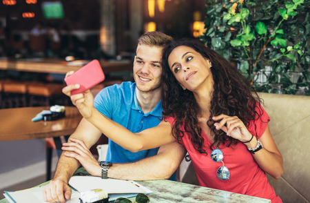 Couple taking photos of themselves with mobile phone in cafe.の写真素材