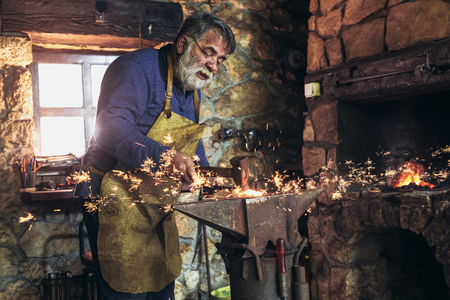 The blacksmith manually forging the molten metal on the anvil in smithy with spark fireworksの写真素材