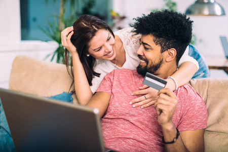 Happy interracial couple shopping online at home, using credit card, laughingの写真素材