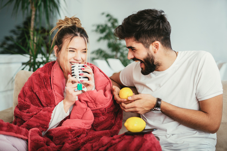Handsome man taking care of his sick girlfriend lying on the sofaの写真素材