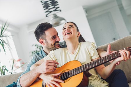 Loving couple with guitar in the room at homeの写真素材