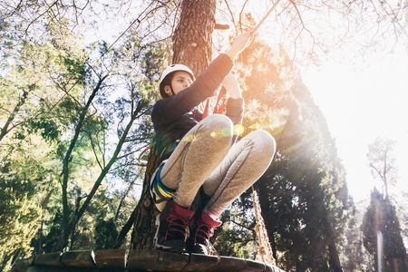 Happy school girl enjoying activity in a climbing adventure park on a sunny dayの写真素材