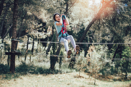 Happy school girl enjoying activity in a climbing adventure park on a sunny dayの写真素材