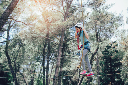 Happy school girl enjoying activity in a climbing adventure park on a sunny dayの写真素材