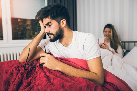 Young upset couple lying separate in a bed, having conflict problemの写真素材