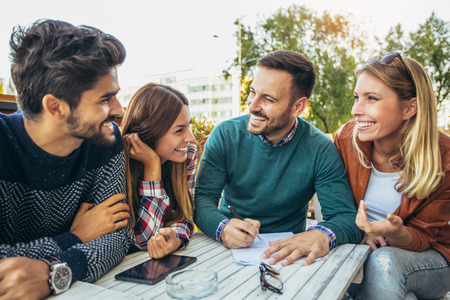 Group of four friends having fun a coffee together. Two women and two men at cafe talking laughing and enjoying their timeの写真素材
