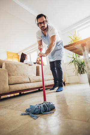 Husband housekeeping and cleaning concept. A man cleans the house, while women gossiping on the sofaの写真素材