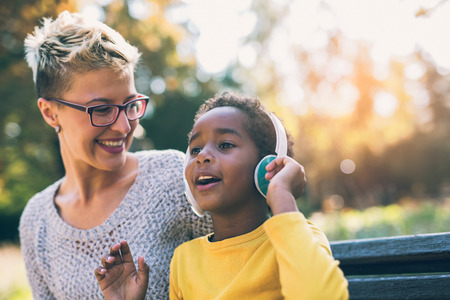 Smiling mother and little daughter having fun, listening to music on headphones. Mixed race family.の写真素材