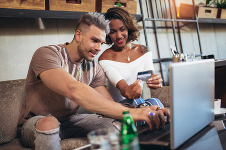 Mixed race couple buying online with credit card and laptop in a coffee shop