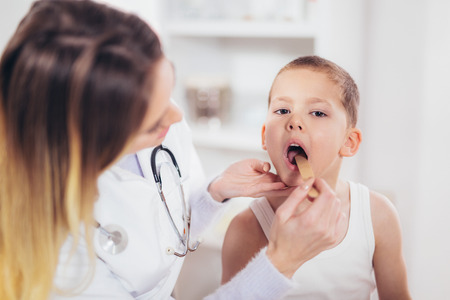 Female doctor examining child with tongue depressor at surgery, medicine, healthcare, pediatry and people conceptの写真素材