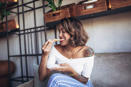 Young cuban woman eating pizza in cafeの写真素材