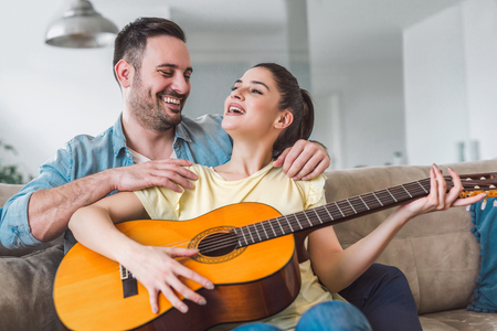 Loving couple with guitar in the room at homeの写真素材