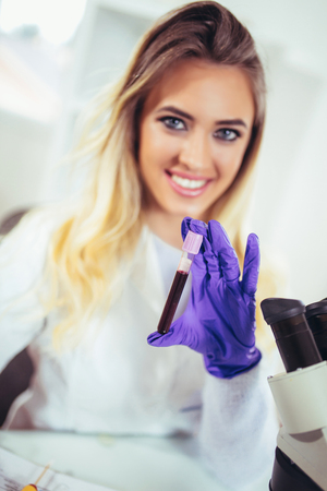Portrait of pretty female laboratory assistant analyzing a blood sample at hospitalの写真素材