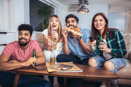 Group of young friends eating pizza and watching tv.Home party.Fast food concept.の写真素材
