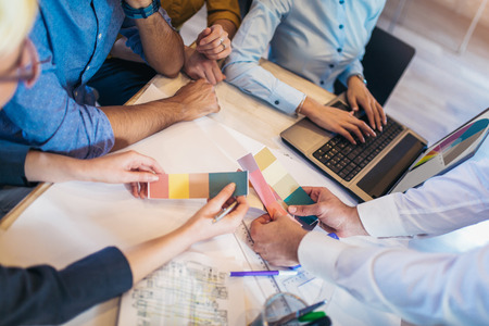 Creative team brainstorming in meeting room. Group of young adults sitting at the table with woman showing color palette to colleagues.の写真素材